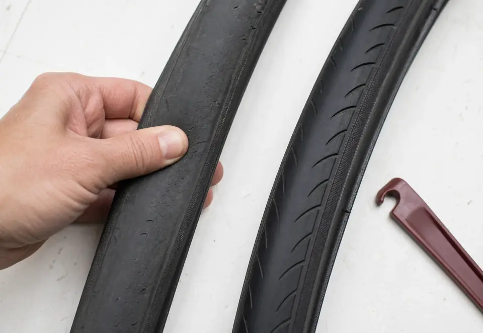 A flattened worn bicycle tire beside a newer tire with healthy tread